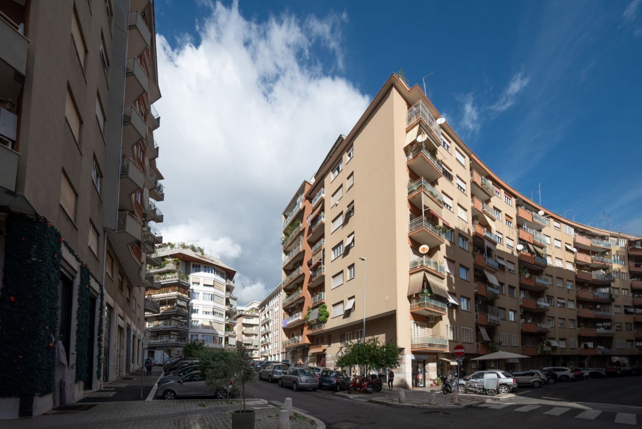 Un immeuble résidentiel à plusieurs étages, doté de balcons, avec un ciel dégagé et des voitures garées dans la rue.