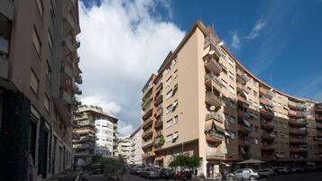 Un immeuble résidentiel à plusieurs étages, doté de balcons, avec un ciel dégagé et des voitures garées dans la rue.