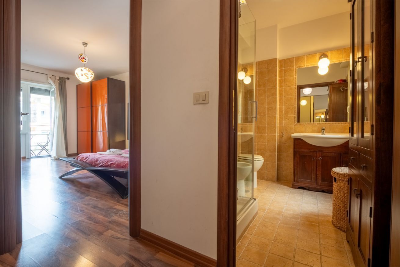 Une salle de bain moderne avec une douche à parois de verre, un meuble-lavabo avec un miroir et un lit dans la pièce adjacente.