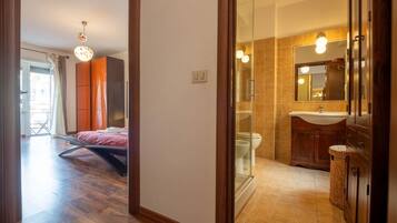 Une salle de bain moderne avec une douche à parois de verre, un meuble-lavabo avec un miroir et un lit dans la pièce adjacente.