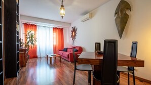 A living room with a red sofa, wooden dining table, and chairs. There is a plant, a lamp, and a wall-mounted decorative piece.