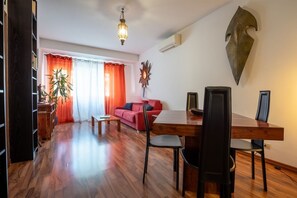 A living room with a red sofa, wooden dining table, and chairs. There is a plant, a lamp, and a wall-mounted decorative piece. - Rialto Apartment Vatican Museums (Rome)