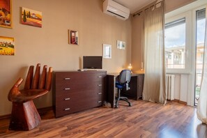 A room with a wooden desk, a chair, a TV, and a window with curtains.