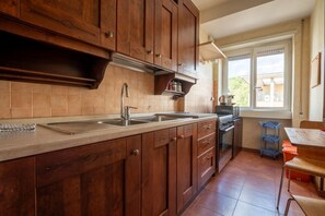 A kitchen with wooden cabinets, a stainless steel sink, and a window overlooking a balcony. - Rialto Apartment Vatican Museums (Rome)