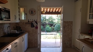 A kitchen with white cabinets, a microwave, and a sink. There is a door leading outside with a view of greenery. - 4 Bed Idyllic Fayence Retreat Private Pool Great Views (Fayence)