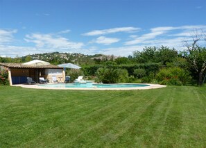 Piscina com espreguiçadeiras e guarda-sóis, cercada por um gramado bem cuidado e árvores.