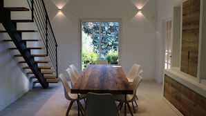 A modern dining area with a wooden table and white chairs, a staircase with black railings, and a large window with a view of greenery. - 4 Bed Idyllic Fayence Retreat Private Pool Great Views (Fayence)