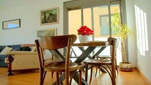Uma sala de estar com uma mesa de jantar de madeira, duas cadeiras, um sofá e um vaso com planta.