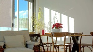 Quarto com sofá, cadeiras de madeira, mesa e plantas em vasos.