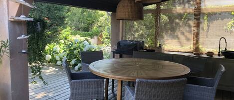 Une terrasse extérieure avec une table ronde en bois et des chaises en osier, entourée de verdure et offrant une vue sur les arbres.