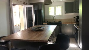 A modern kitchen with a wooden island, black chairs, a sink, and a stove. - 5 bedroom VILLA with pool on a hillside near AIX  (Mimet)