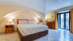A bedroom with a large bed, two bedside tables, a dresser, and a balcony with curtains. - Opera House Suite with Balcony (Catania)