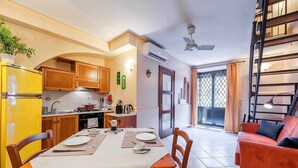 A compact kitchen with wooden cabinets, a yellow refrigerator, and a dining area with a table set for two. - Opera House Suite with Balcony (Catania)