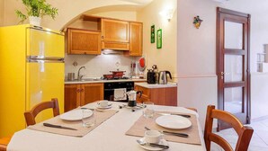 A compact kitchen with wooden cabinets, a yellow refrigerator, and a dining table set for two. - Opera House Suite with Balcony (Catania)