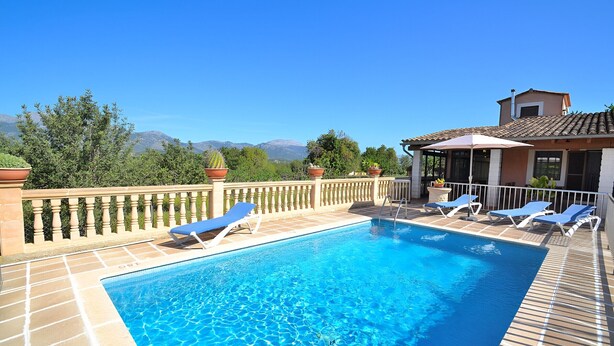 Una piscina rectangular con agua azul cristalina, rodeada por un solárium con baldosas. Hay sillas de descanso y un pérgola con techo.