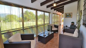 Un salón amplio con mobiliario de mimbre, ventanas grandes y vista a zonas verdes.