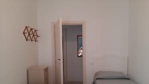 A bedroom with two beds, a wardrobe, and a door leading to another room.