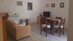 A living room with a sofa, a dining table with chairs, a TV, and framed pictures on the wall.