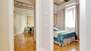 A bedroom with a bed, wooden flooring, a ceiling with exposed beams, and a window with curtains. - COLOSSEUM ELEGANT APARTMENT FOR 4 - NEAR METRO (Roma)