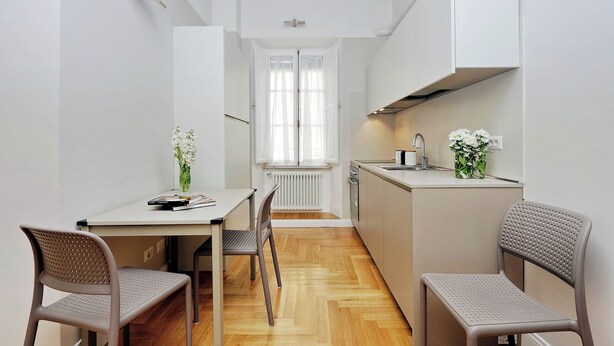 A narrow kitchen with a dining table and chairs, a window with curtains, and a radiator. - COLOSSEUM ELEGANT APARTMENT FOR 4 - NEAR METRO (Roma)
