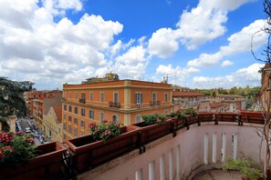 Un balcón con macetas de terracota y flores, con vista a una calle con coches estacionados y edificios.
