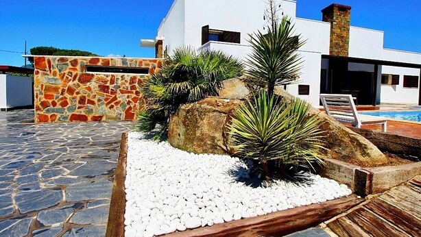 A modern house with a stone wall, white exterior, and a pool area.