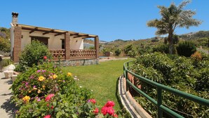A building with a balcony, surrounded by a garden with various flowers and a palm tree. - 1076 Cortijo de la Musica (Frigiliana)