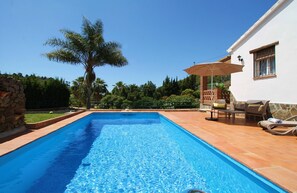 Une piscine rectangulaire à l’eau d’un bleu limpide, entourée d’une terrasse carrelée aménagée avec du mobilier d’extérieur et un palmier.