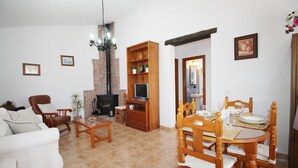 A living room with a sofa, chairs, a dining table set for four, a fireplace, and a television. - 1076 Cortijo de la Musica (Frigiliana)