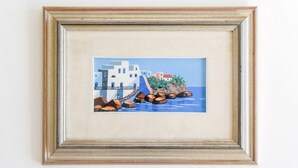 A framed painting of a coastal scene with buildings and rocks.