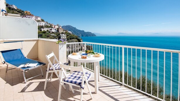 A balcony with a table and chairs overlooking a coastal view.