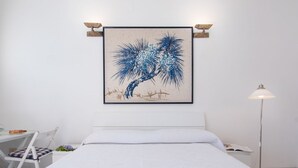 A bedroom with a bed, a desk, and a chair. There is a framed artwork on the wall above the bed.