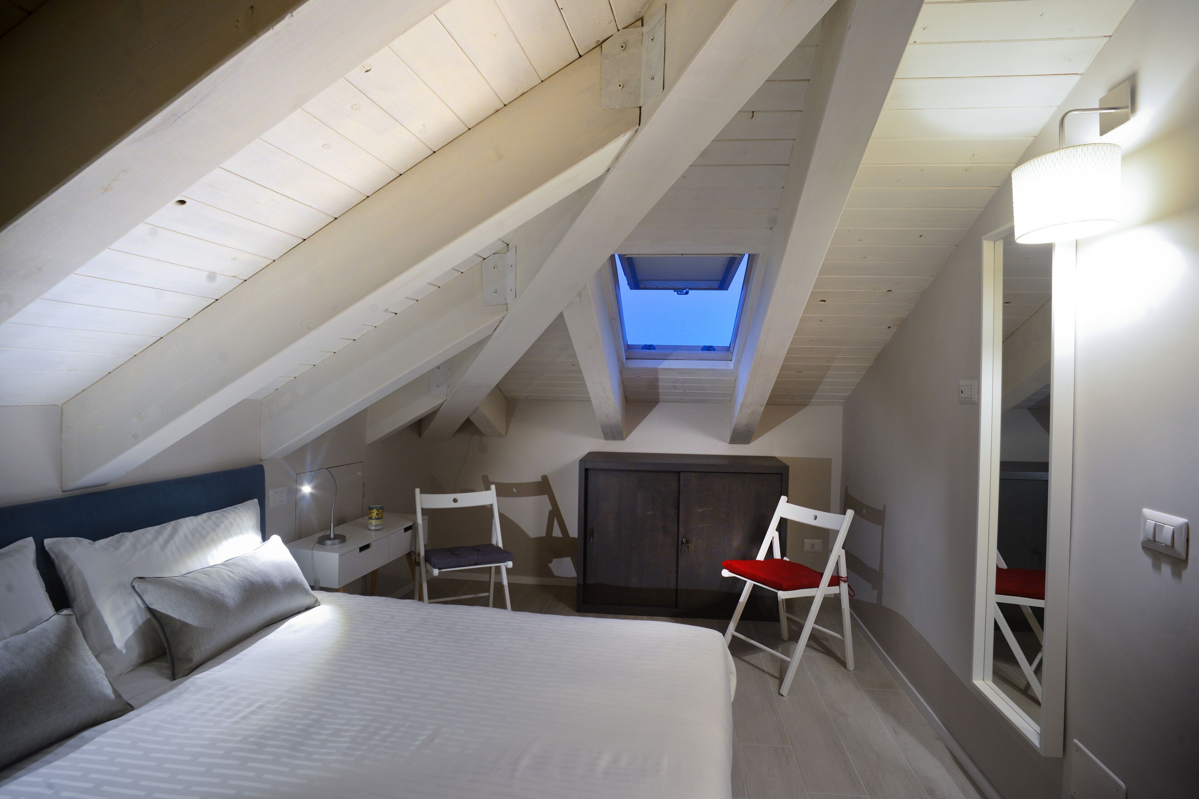 Camera da letto con soffitto spiovente, un lucernario, un letto, due poltrone, una scrivania e un armadio.