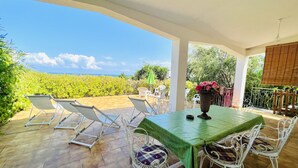 Un patio cubierto con una mesa y sillas, vista a un viñedo y cielo despejado.