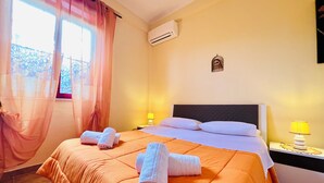 Habitación de hotel con cama, dos lámparas de noche, unidad de aire acondicionado y ventana con cortinas.