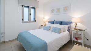 A bedroom with a bed, bedside tables, a window with blinds, and wall art.