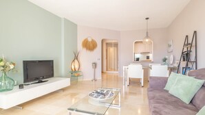 A modern living room with a flat-screen TV, a glass coffee table, a sofa, and a kitchen area in the background. - Luxury Holiday Rental (Las Lagunas de Mijas)