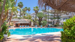 A swimming pool with lounge chairs, surrounded by palm trees and a thatched-roof hut. - Luxury Holiday Rental (Las Lagunas de Mijas)