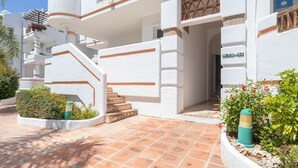 A white building with a staircase leading to a balcony, a door with a geometric window, and a sign with numbers. - Luxury Holiday Rental (Las Lagunas de Mijas)