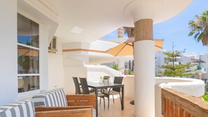 A modern outdoor seating area with a glass table and chairs, a striped sofa, and a large umbrella. - Luxury Holiday Rental (Las Lagunas de Mijas)