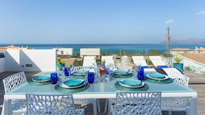 Une table à manger dressée avec de la vaisselle en verre bleue et des assiettes, offrant une vue sur la côte.