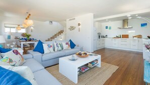 A modern living room with a sofa, coffee table, and a staircase leading to a kitchen area.
