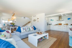 A modern living room with a sofa, coffee table, and a staircase leading to a kitchen area. - Modern House With Panoramic Sea Views in Mallorca (Son Serra de Marina)