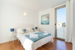 A bedroom with a bed, bedside tables, a painting, and a view through a glass door.