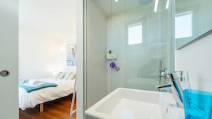 Une chambre d’hôtel comprenant un lit, une salle de bain avec un lavabo et un miroir, ainsi qu’un espace douche.