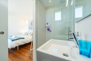 A hotel room with a bed, a bathroom with a sink and mirror, and a shower area.