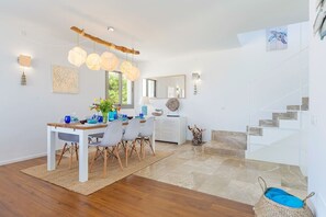 Ein moderner Essbereich mit einem Holztisch, weißen Stühlen und einer hängenden Leuchte.