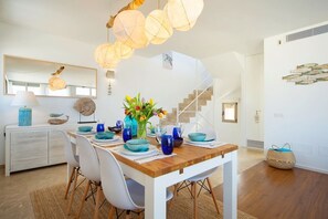 A dining area with a wooden table, white chairs, and blue tableware. - Modern House With Panoramic Sea Views in Mallorca (Son Serra de Marina)