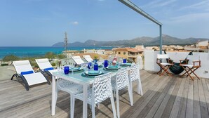 Un coin repas avec une table dressée pour deux personnes, offrant une vue sur la côte et les montagnes au loin.