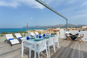 A dining area with a table set for two, overlooking a coastal view with mountains in the distance.
